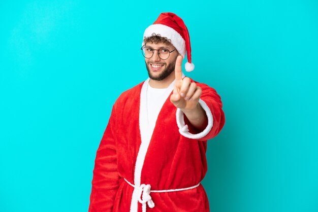 Young man disguised as santa claus isolated on blue background showing and lifting a finger