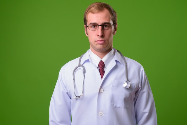 Young man doctor against green wall