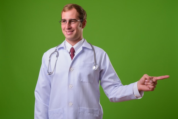 Young man doctor against green wall