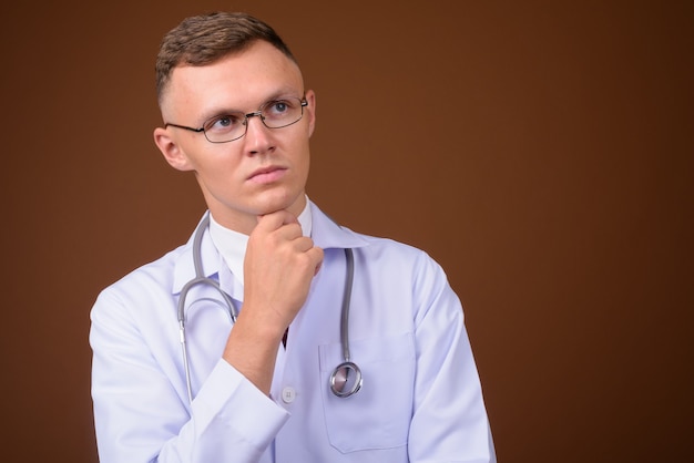 Young man doctor wearing eyeglasses against brown background