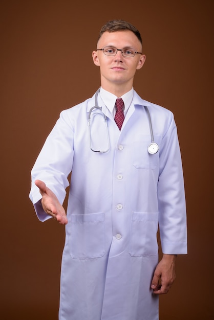 Young man doctor wearing eyeglasses against brown background