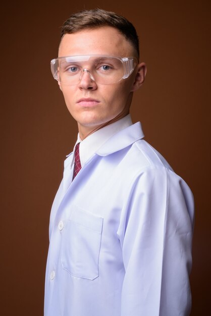 Young man doctor wearing protective glasses against brown backgr