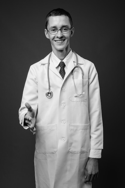  young man doctor with eyeglasses against gray wall in black and white