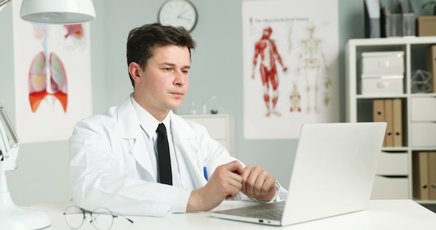 Young man doctor working with laptop in light cabinet. 