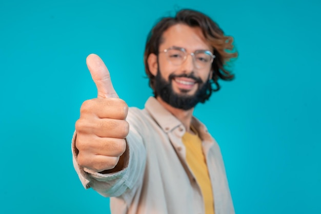 Young man doing happy thumbs up gesture with hand standing over isolated blue background