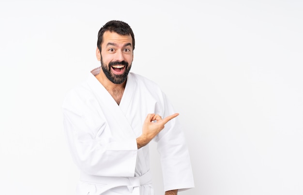 Young man doing karate over isolated white surprised and pointing side