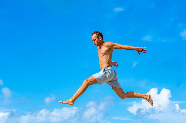 Young man doing parkour jump on the blue sky background on sunny summer day