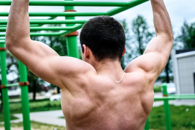 Young man doing pull ups on horizontal bar outdoors on sports playground. Street workout.