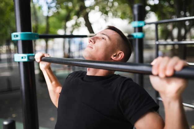 Giovane che fa pull up sulla barra orizzontale all'aperto, allenamento, concetto di sport.