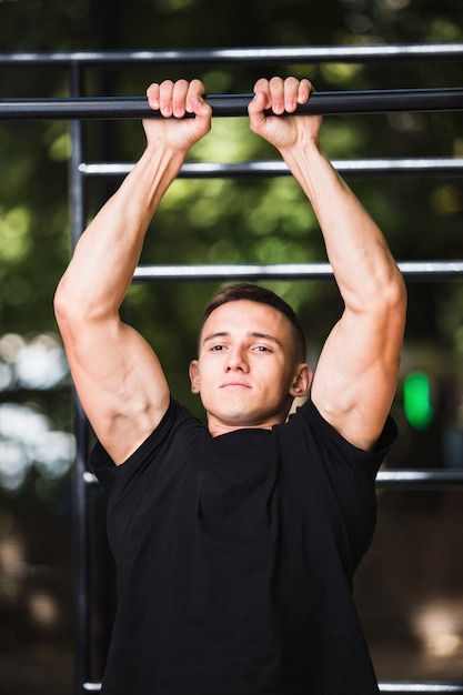 Photo young man doing pull ups on horizontal bar outdoors, workout, sport concept.