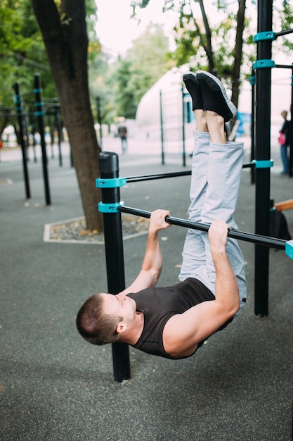 Young man doing pull ups on horizontal bar outdoors, workout, sport concept.