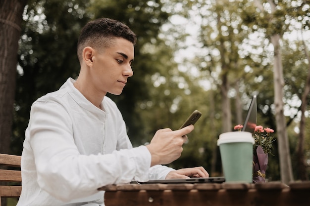 Young man doing work remotely from a park. Freelancer working outside.