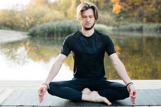 Young man doing yoga asana in nature near the lake