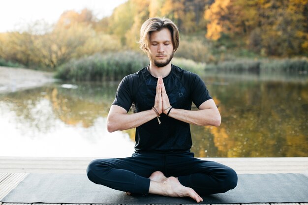 Young man doing yoga asana in nature near the lake