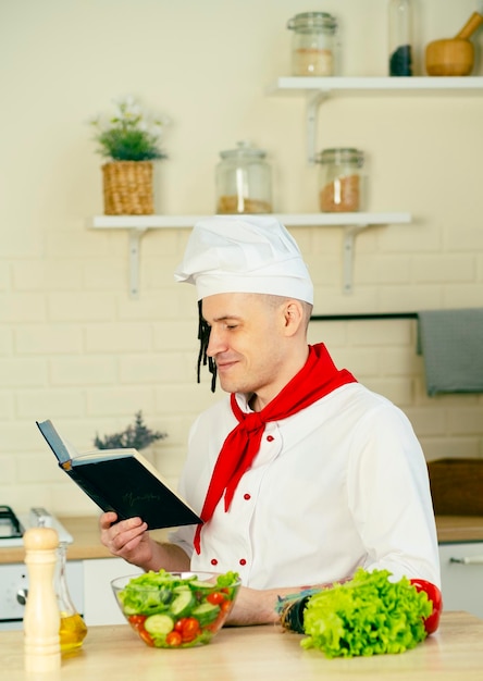 Young man dressed as chef reading recipe book in kitchen Concept of food cooking recipes