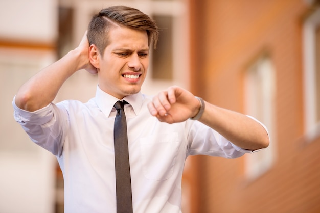 若い男は遅く実行している時計を見てフォーマルな服を着た。