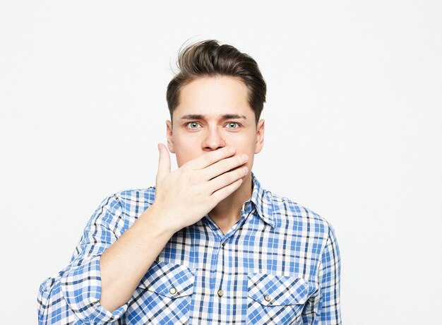 A young man dressed in a plaid blue shirt covers his mouth with his palms