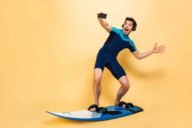 Young man dressed in swimsuit make selfie by phone listening music with headphones