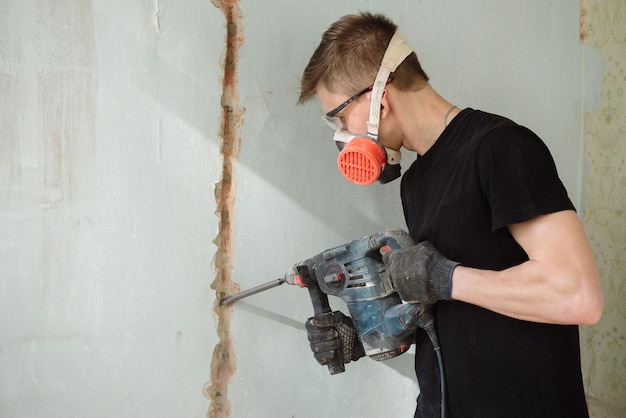 Un giovane perfora un muro con un perforatore