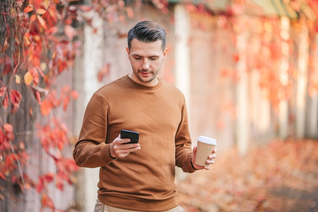 Young man drinking coffee in autumn park outdoors