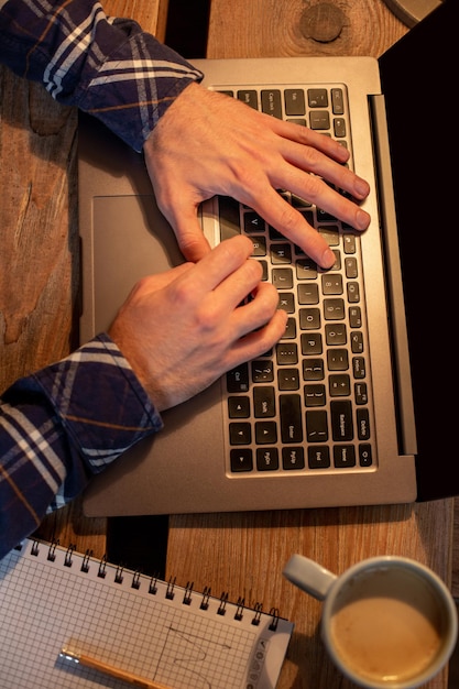 카페에서 커피를 마시고 노트북을 사용하는 젊은 남자는 커피 휴식 시간에 노트북을 사용하여 손을 사용합니다.
