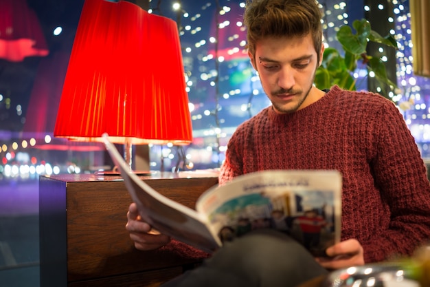 Young man drinking coffee and reading news on sofa