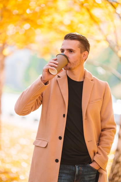 Молодой человек пьет кофе с телефона в Осенний парк на открытом воздухе