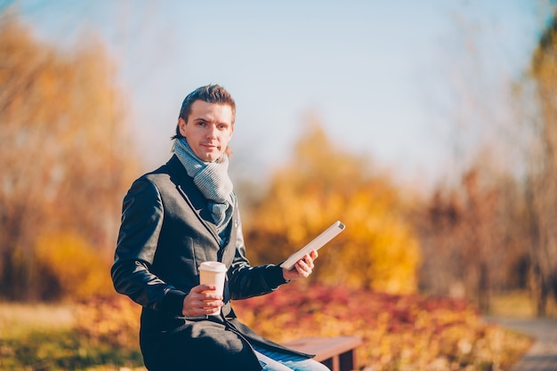 Young man drinking coffee with phone in autumn park outdoors