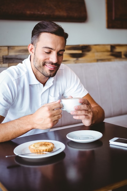 Young man drinking cup of coffee and pastry beside