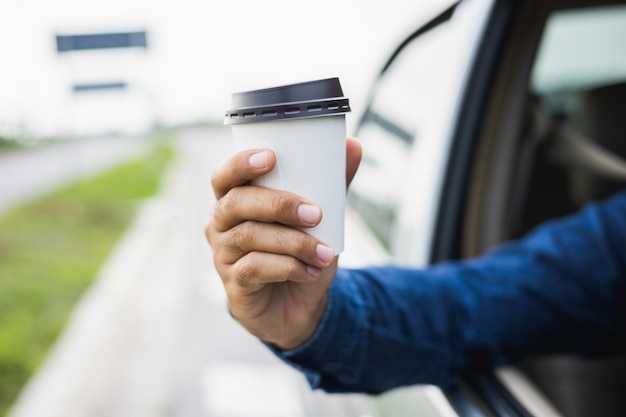 Young man drinking a cup of hot coffee while driving car to travel Hands holding steering wheel Take a break for a refreshing coffee before your trip