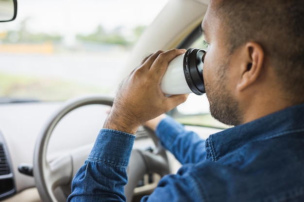 Young man drinking a cup of hot coffee while driving car to travel Hands holding steering wheel