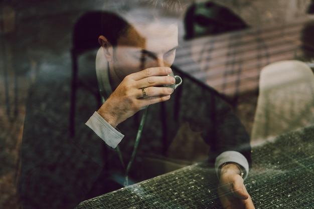 young man drinking drink seen through window