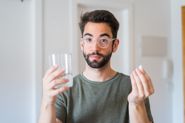 Young man drinking medicine at home