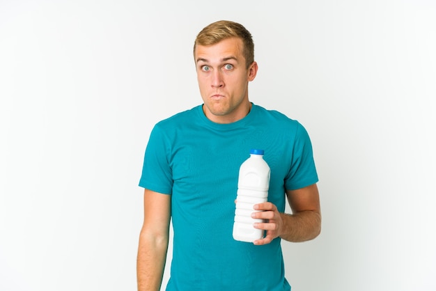 Young man drinking milk shrugs shoulders and open eyes confused