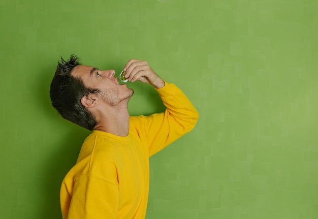 Foto giovane che beve olio d'oliva in una piccola ampolla di plastica su uno sfondo verde stile di vita sano