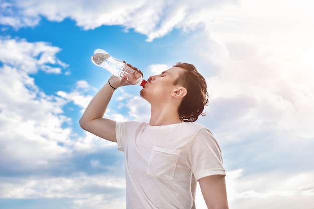Молодой человек пьет воду из бутылки