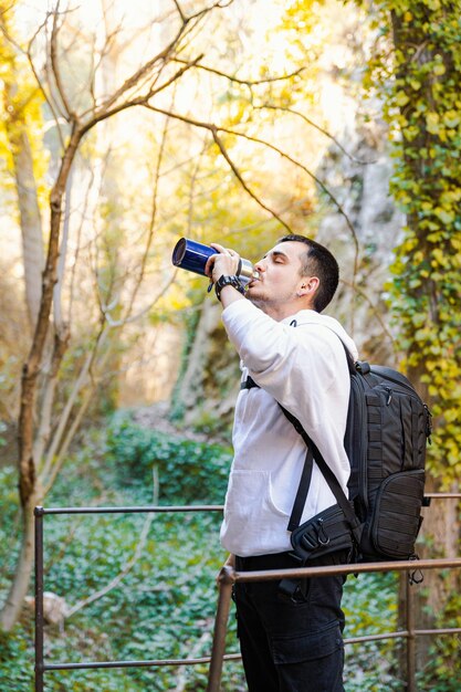 Young man drinking water from a refillable bottle, in the forest, ecological and sport concept