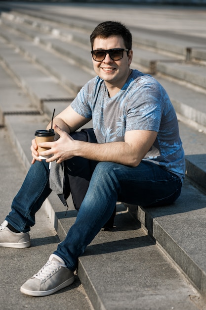 A young man drinks coffee in the city and walks outside.