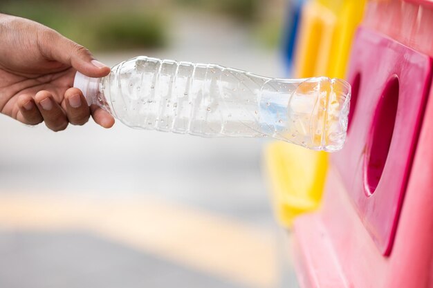 若い男がペットボトルを飲み、ゴミ箱に捨てます。環境の日に関するビデオプラスチック廃棄物を正しいカテゴリに分けます。公共のゴミ