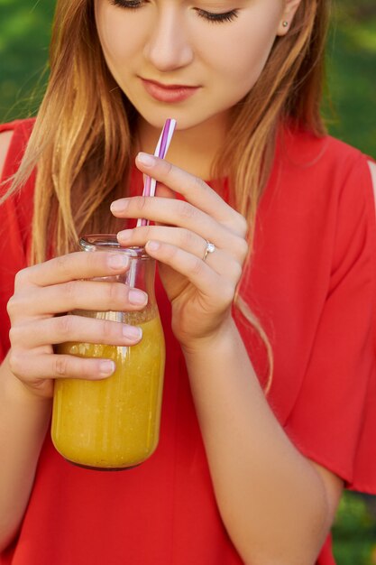 Young man drinks healthy detox smoothie with juice on green park background.