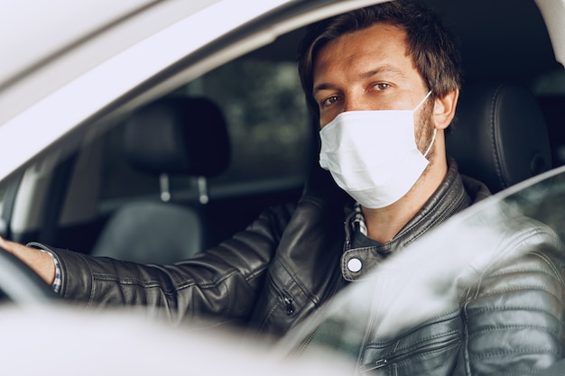 Young man driving car in medical mask