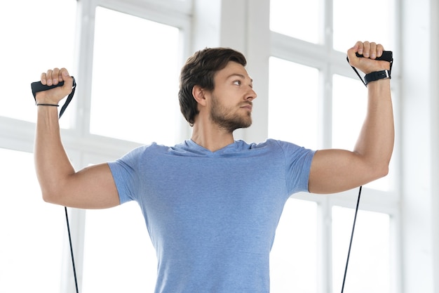 Photo young  man during workout with a resistance rubber bands in the gym. standing shoulder press exercise.