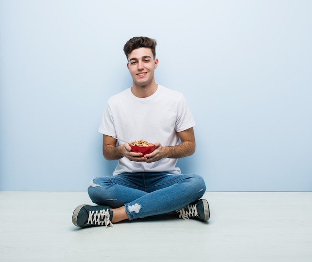 Young man eating cereals sitting on the floor happy, smiling and cheerful.