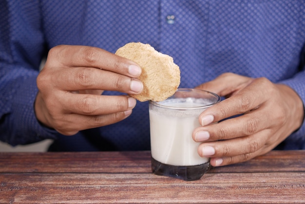 Young man eating cookies and glass of milk on table