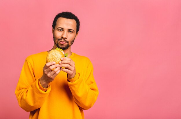 Young man eating hamburger isolated over pink