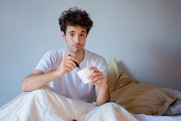 Young man eating ice cream in bed