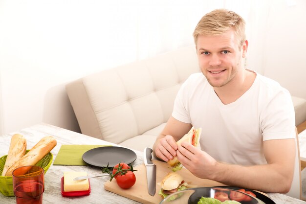 若い男が自宅でサンドイッチを食べる