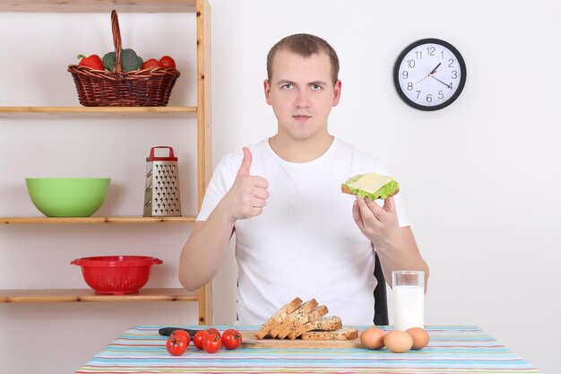 Young man eating sandwich and milk in the kitchen