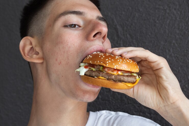 若い男は路上でハンバーガーを食べる、若い世代へのファーストフードの悪影響の概念、クローズアップ