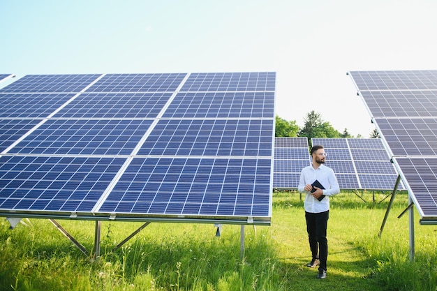 Молодой человек-инженер в белой рубашке держит планшет и проверяет фотоэлектрические панели на солнечной электростанции Скопируйте место для текста